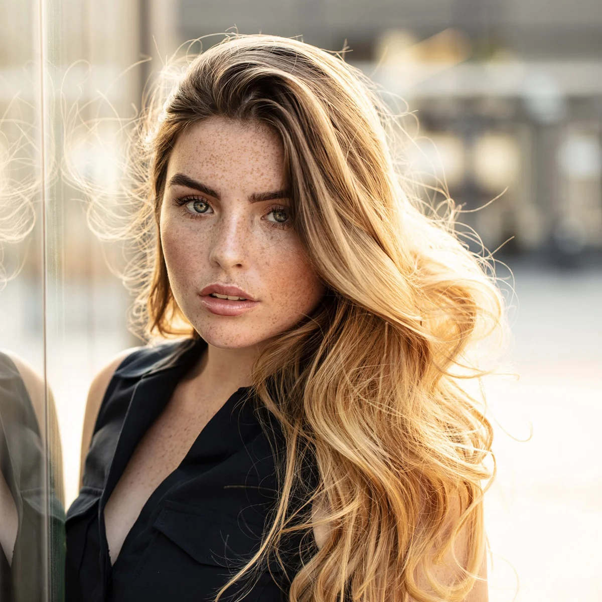 Woman leaning against a glass wall with the sun shining behind her